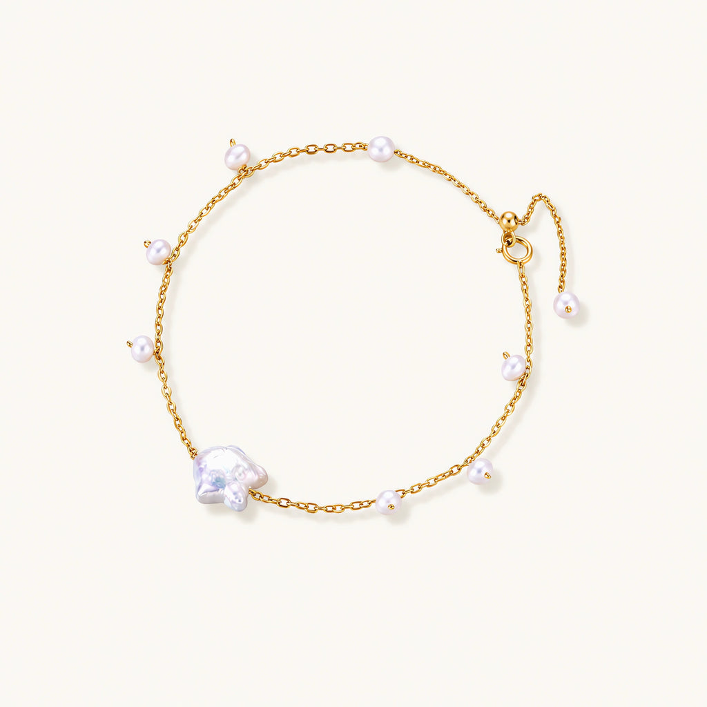 Delicate gold chain bracelet with baroque pearl centerpiece and small freshwater pearls on cream background.