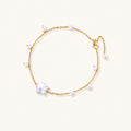 Delicate gold chain bracelet with baroque pearl centerpiece and small freshwater pearls on cream background.