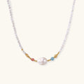 Dainty white beaded necklace with a central freshwater pearl, peach and blue beads and gold vermeil accents on a cream background.