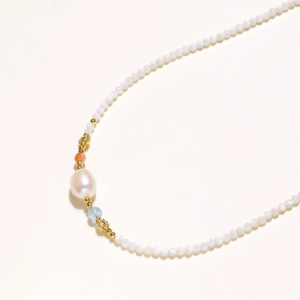 Dainty white beaded necklace with a central freshwater pearl, peach and blue beads and gold vermeil accents on a cream background.