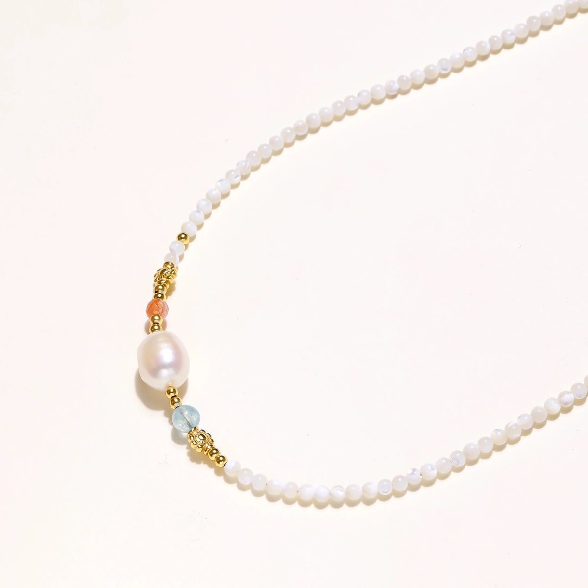 Dainty white beaded necklace with a central freshwater pearl, peach and blue beads and gold vermeil accents on a cream background.
