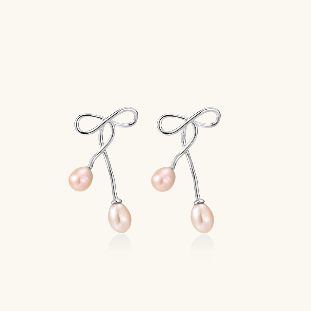 Rhodium-plated silver earrings with organic vine curves and two peachy freshwater pearls on cream background