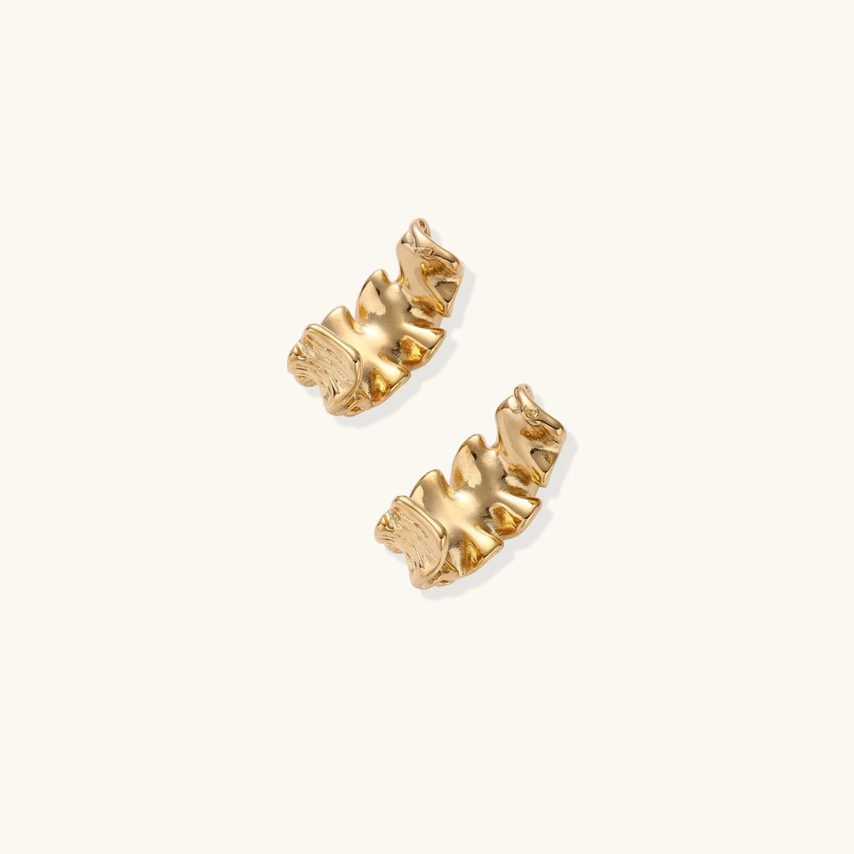 Pair of gold huggie hoops with sculpted wave texture and dimensional ripples on neutral background.