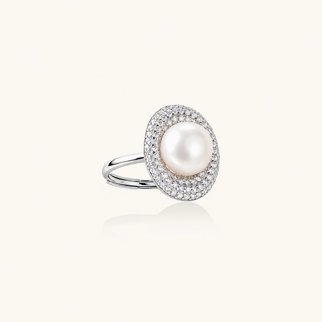 Silver ring with lustrous white pearl center surrounded by sparkling crystal halo on light background.