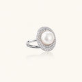 Silver ring with lustrous white pearl center surrounded by sparkling crystal halo on light background.