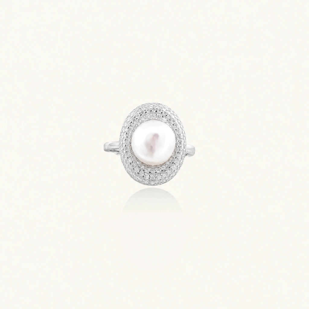 Silver ring with lustrous white pearl center surrounded by sparkling crystal halo on light background.
